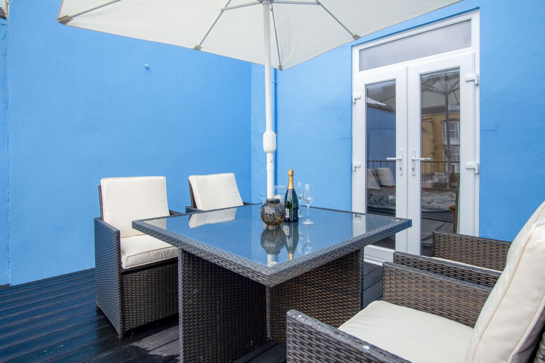 Een glazen tafel met rieten stoelen en een witte parasol.