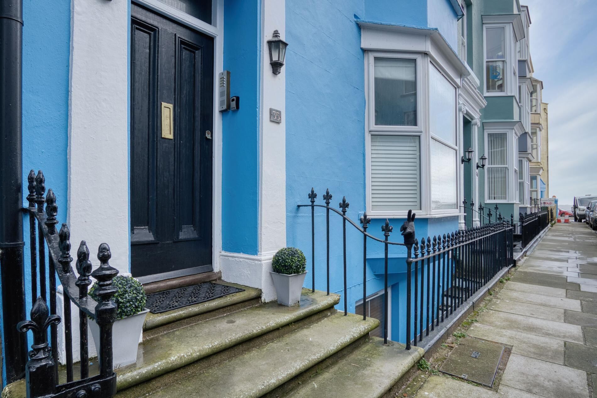 Una fila de casas escalonadas con fachadas azules y blancas, un portón de hierro negro y una pequeña planta en maceta en los escalones.