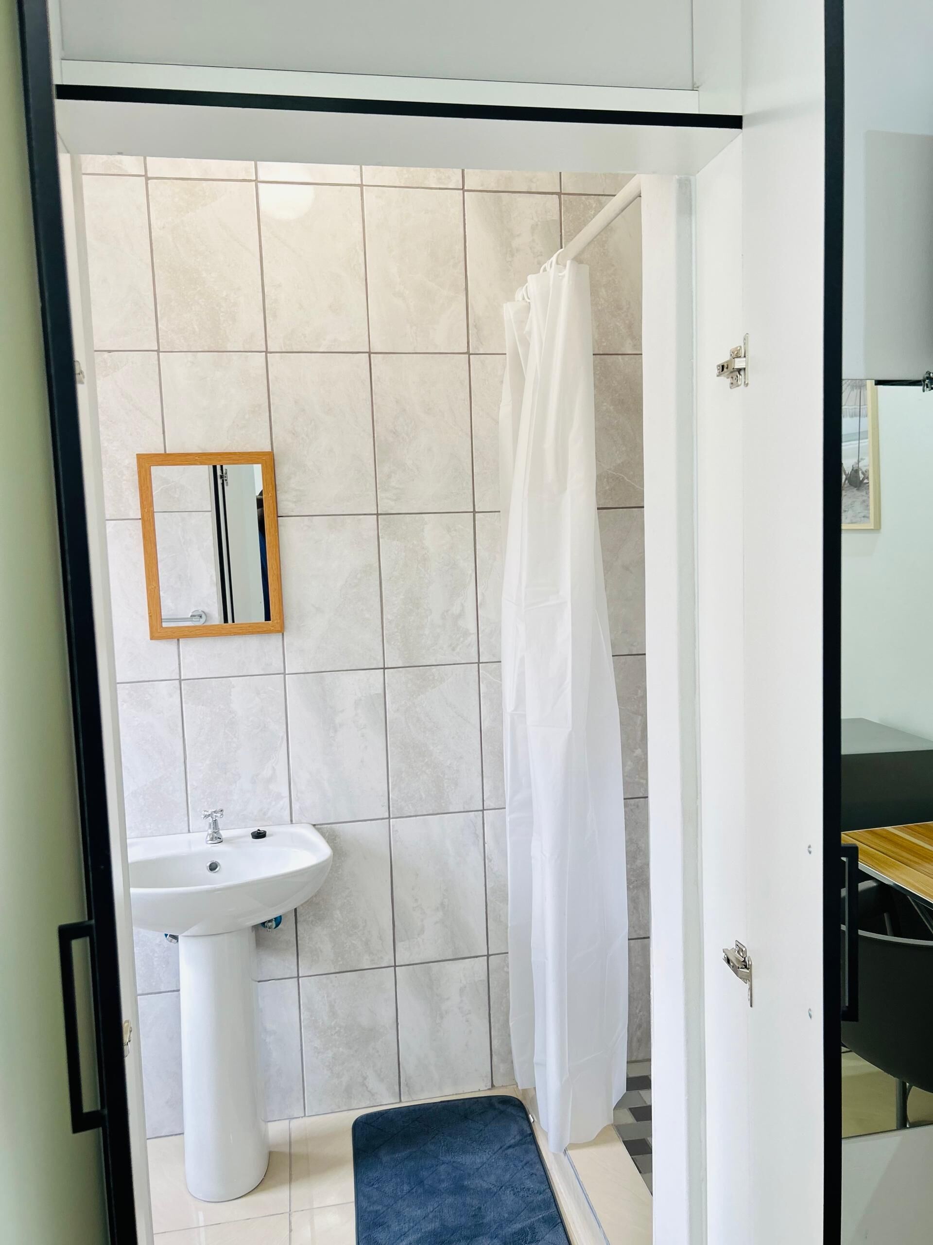 Un baño con lavamanos blanco, un espejo y una ducha con cortina blanca.