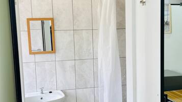 Un baño con lavamanos blanco, un espejo y una ducha con cortina blanca.