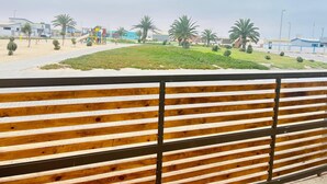 Ein Holzzaun mit horizontalen Lamellen, eine Rasenfläche mit Palmen und ein Spielplatz im Hintergrund.