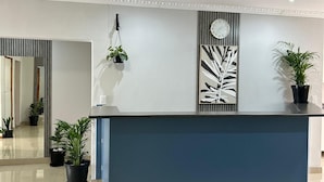 Ein Empfangsschalter mit blauer Theke, Zimmerpflanzen, einer Uhr und einer dekorativen Wandverkleidung.