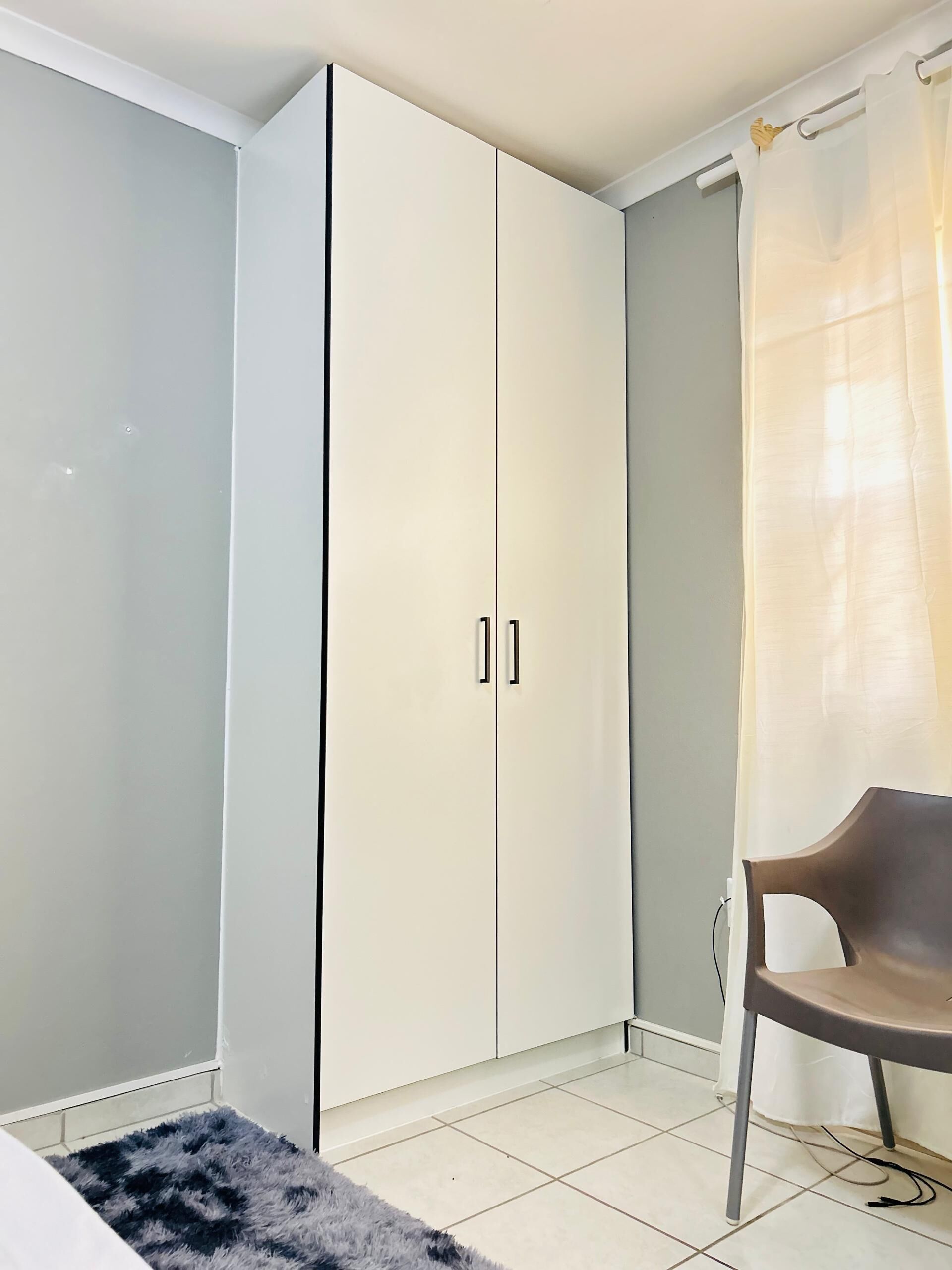 A room with a wardrobe, a chair, and a rug.