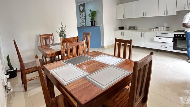 Ein Essbereich mit einem Holztisch und Stühlen, eine Küche mit weißen Schränken und ein Blumentopf.