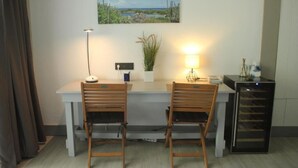 Una habitación pequeña y moderna con un escritorio, dos sillas, una lámpara, una planta pequeña y un refrigerador.
