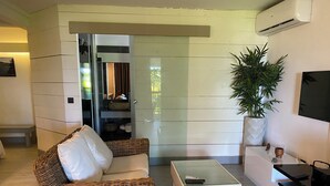 Una sala de estar moderna con un sofá de mimbre, una mesa de centro de vidrio, un televisor y una planta en maceta.