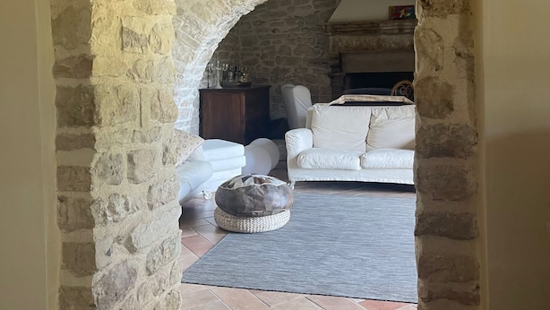 Ein rundbogiger Steineingang führt in ein Wohnzimmer mit einem weißen Sofa und einem runden Teppich.