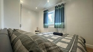 Quarto com cama, mesa de cabeceira, janela com cortinas e radiador.