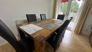 Mesa de jantar de madeira com quatro cadeiras, um radiador e vista para um jardim através de uma porta de vidro.