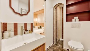 Een moderne badkamer met een grote spiegel, een witte wastafel en een toilet. Op de muur is een houten paneel ontwerp en er is een klein plankje met toiletartikelen.