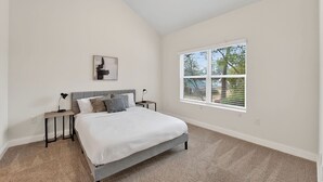 Une chambre à coucher avec un lit, des tables de chevet, une lampe, un tableau et une fenêtre avec des stores.