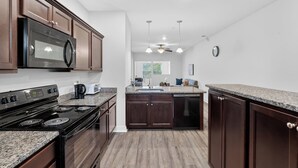 Une cuisine moderne avec des meubles en bois foncé, une cuisinière noire et des plans de travail en granit.