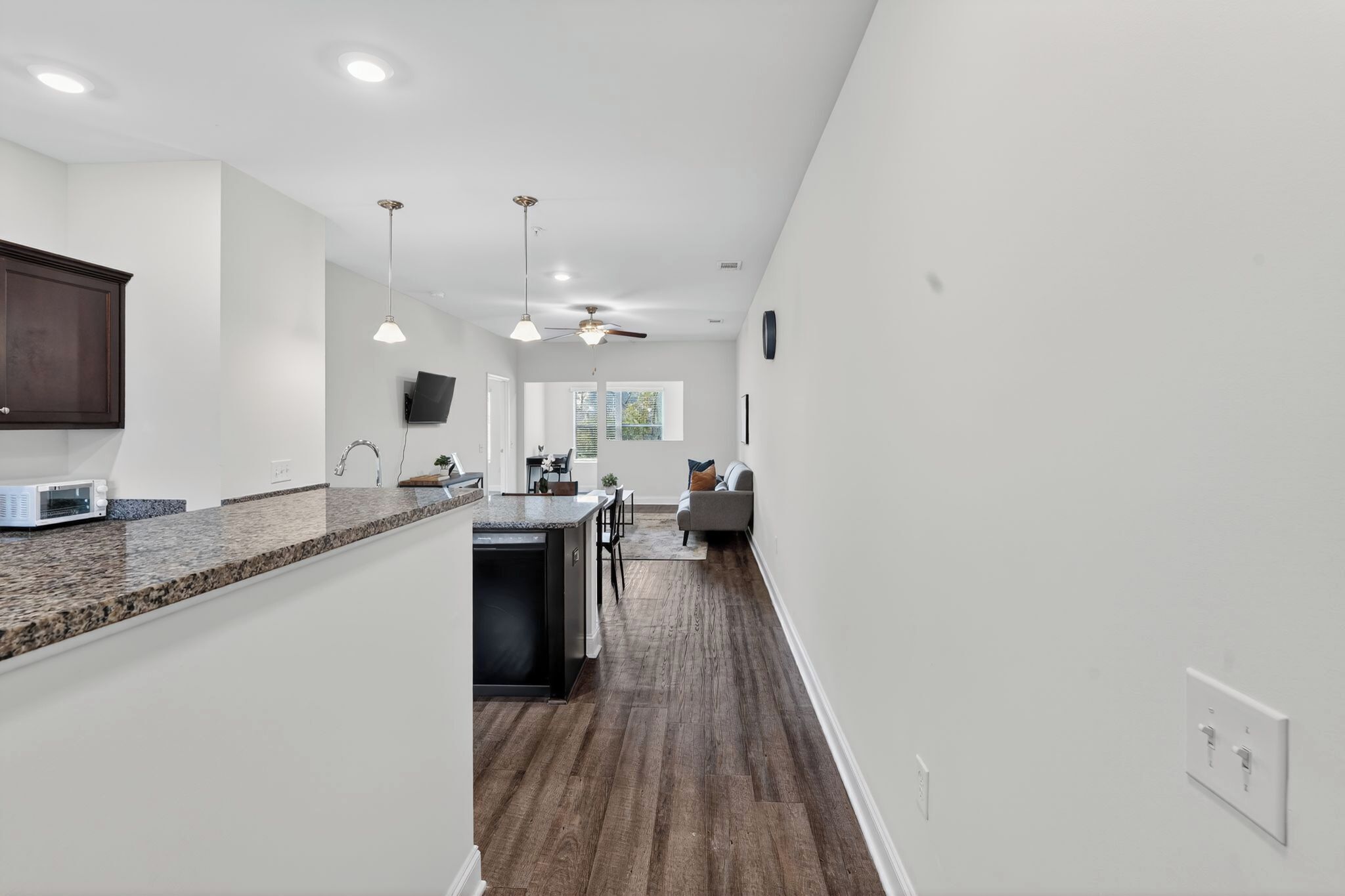 A modern kitchen with granite countertops, a built-in microwave, and a dining area with a gray sofa and a ceiling fan.