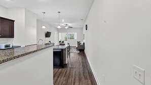 Une cuisine moderne dotée de plans de travail en granit, d’un four à micro-ondes encastré et d’un coin repas avec un canapé gris et un ventilateur de plafond.