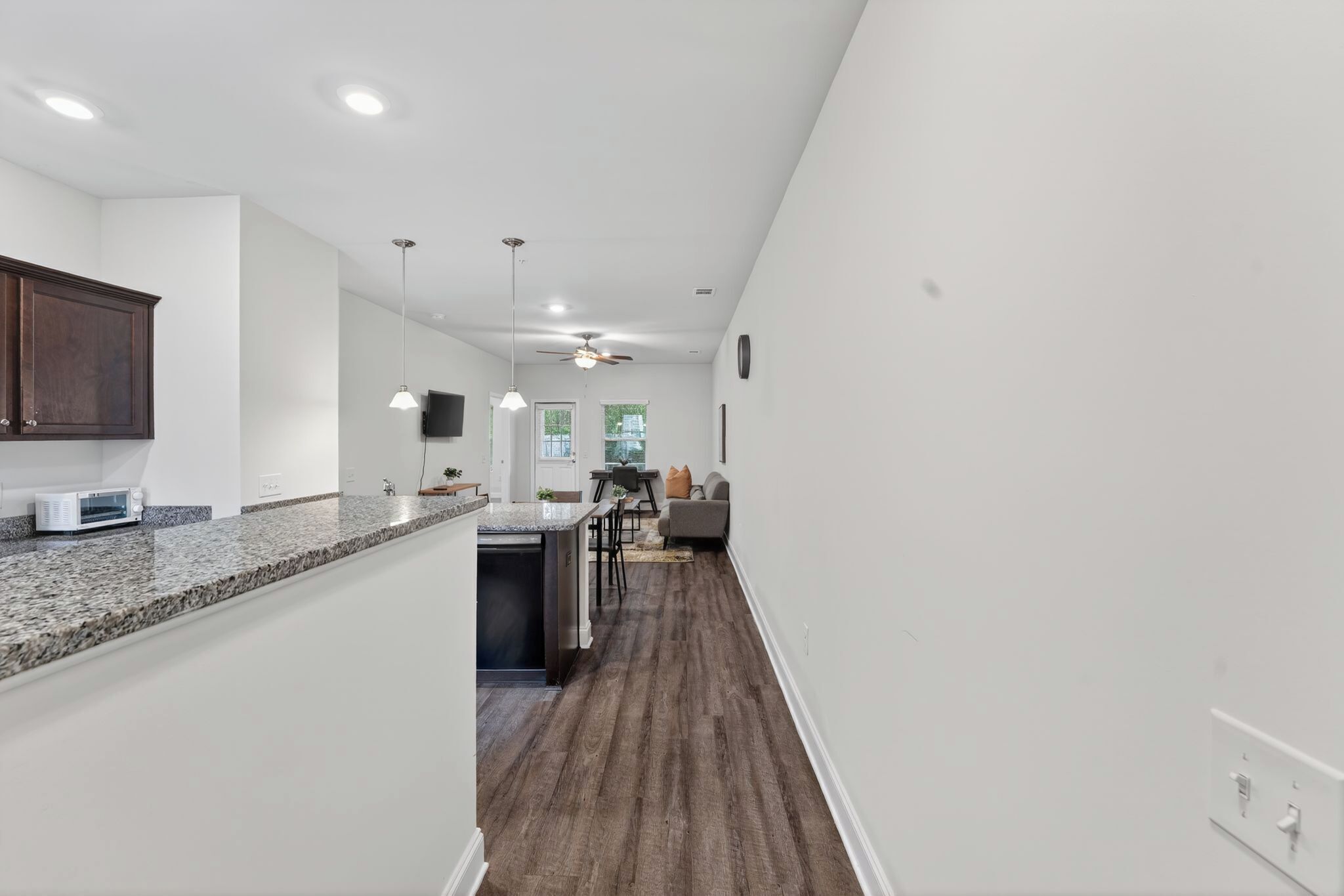 A modern kitchen with a granite countertop, a microwave, and a ceiling fan.