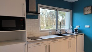 Een moderne keuken met witte kasten, een zwarte magnetron, een raam met uitzicht op bomen, een koffiezetapparaat en een broodrooster.