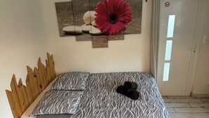 Een slaapkamer met een bed, een houten hoofdbord, een bed met een patroon en een kunstwerk met bloemen en stenen.
