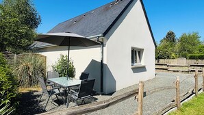 Een huis met een schuin dak, een klein raam en een terras met een tafel en stoelen.