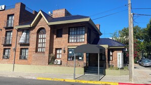 A two-story brick building with a covered entrance and a sign indicating it is a hotel. - HOTEL AYRES (Colonia del Sacramento)