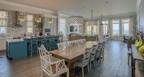 Une cuisine spacieuse dotée d’un îlot central, un coin repas avec une grande table en bois et une vue sur la mer grâce à de grandes fenêtres.