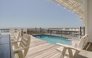 Une terrasse en bois avec une piscine, des chaises blanches et une vue sur l’océan.