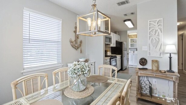 A dining area with a glass-top table, wicker chairs, and a hanging light fixture. - Ground Level Private Beach Home w/Pool & Beach Access- Adorable and affordable! (Gulf Shores)