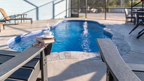 A poolside area with a lounge chair, a small table with a book, glasses, and a cup of coffee. - Ground Level Private Beach Home w/Pool & Beach Access- Adorable and affordable! (Gulf Shores)