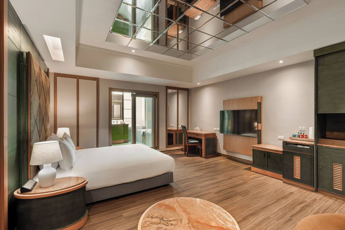 A modern hotel room with a large bed, a desk, a TV, and a seating area.