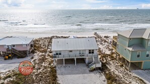 Una propiedad frente a la playa con una casa central, un porche cubierto y una escalera que lleva a una terraza.