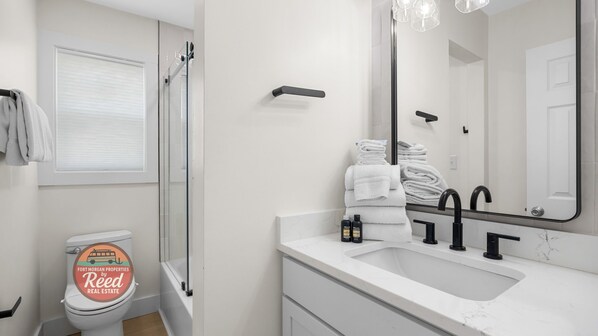A modern bathroom with a toilet, shower, sink, and a large mirror. - Adorable Family Home With Amazing Beach Views (Gulf Shores)