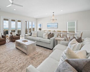 A spacious living room with a large sofa, coffee table, and chairs, a chandelier, and a view of the ocean through large windows. - West Side Gorgeous 6 Br 4.5 Ba Beach Front Duplex - Newly Renovated! (Gulf Shores)