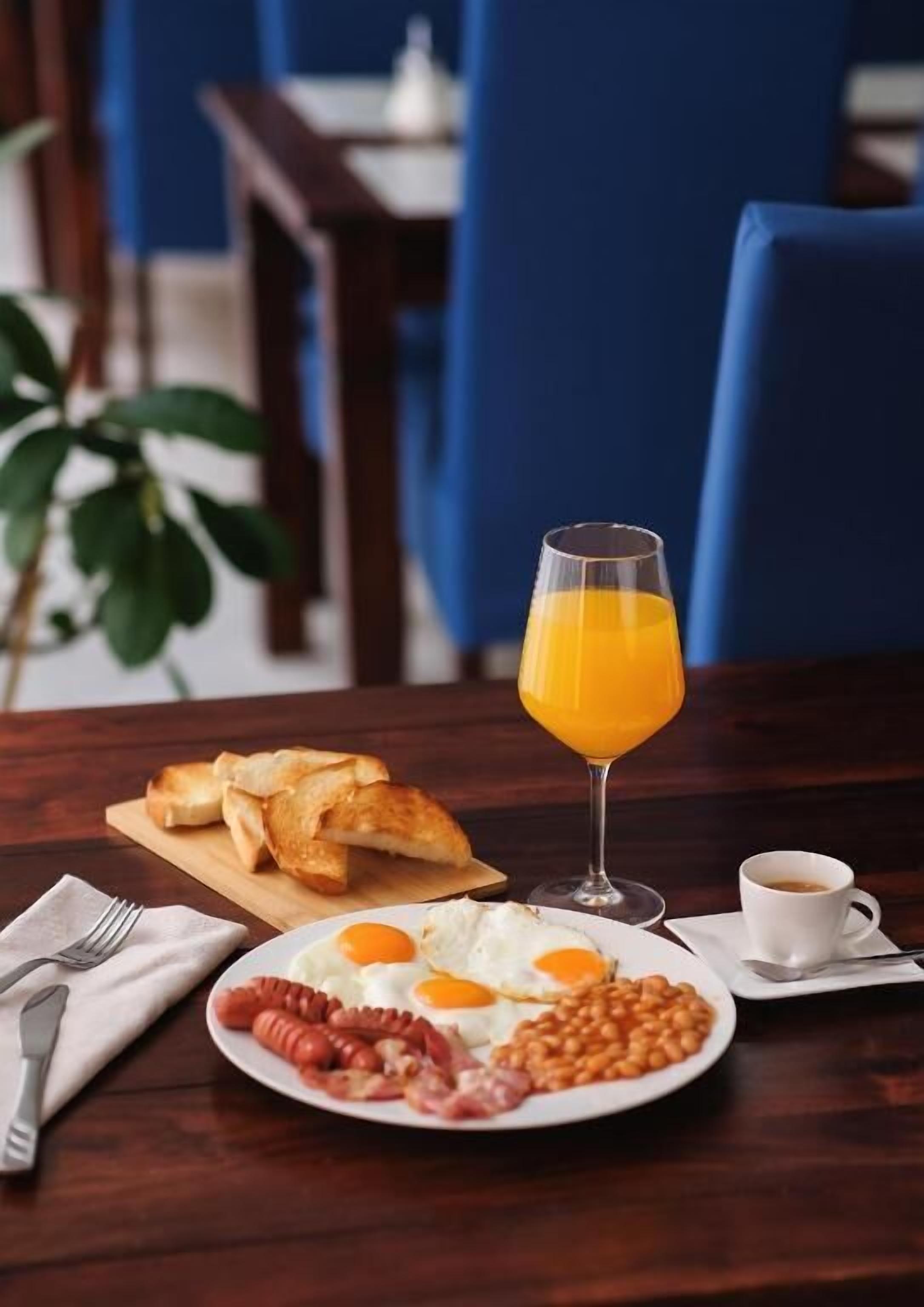Ein Frühstückstisch mit Toast, Eiern, Bohnen, Würstchen, einem Glas Orangensaft und einer Tasse Kaffee.