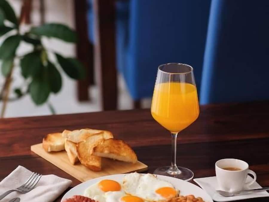A breakfast setting with toast, eggs, beans, sausages, a glass of orange juice, and a cup of coffee on a wooden table.