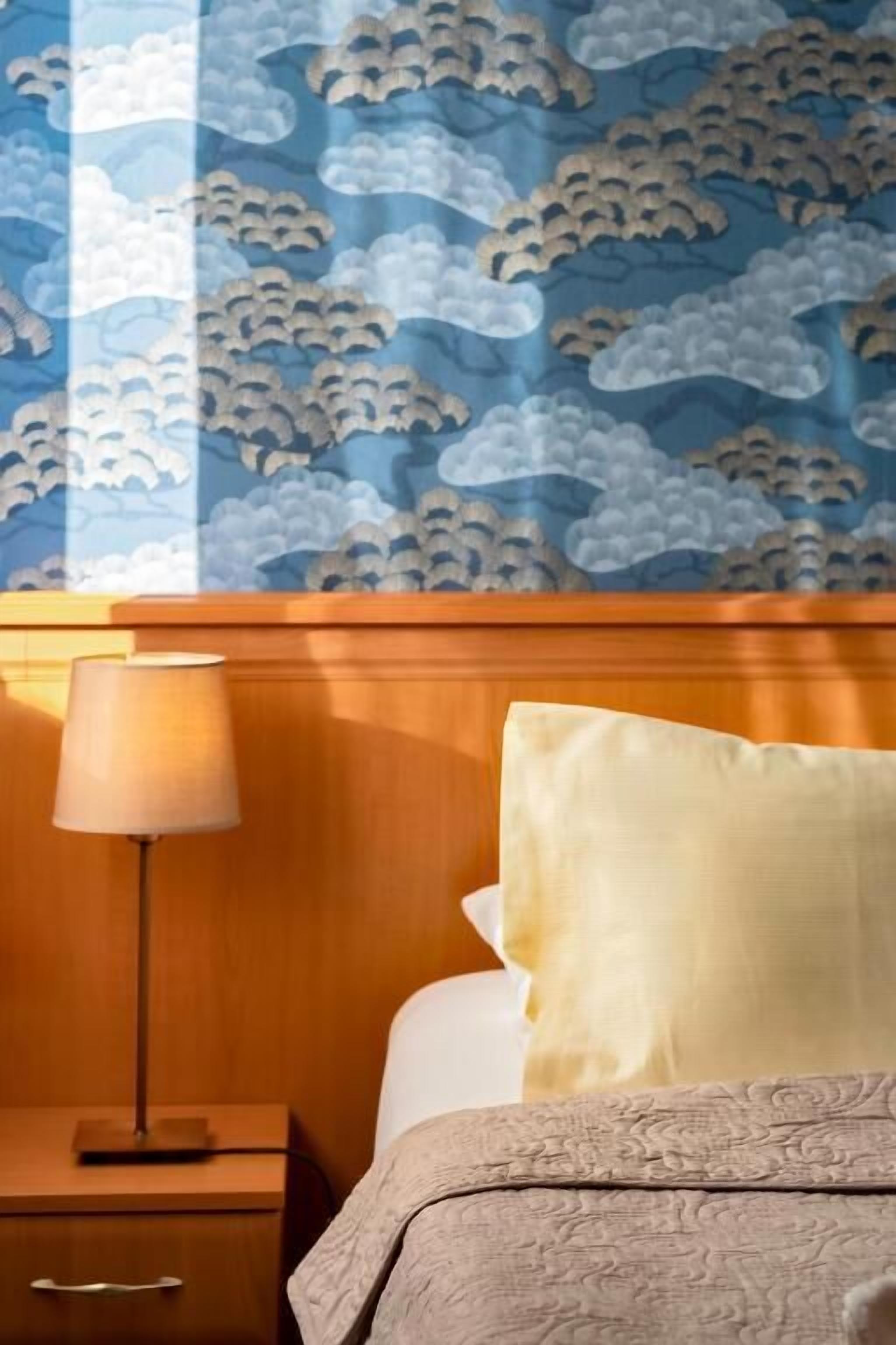 A hotel room with a wooden headboard, a bedside lamp, a nightstand, and a bed with a patterned bedspread.