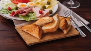 A meal with a plate of food, a glass of orange juice, and a wooden board with bread. - König Hotel (Pécs)