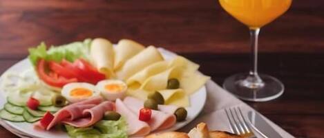A meal with a plate of food, a glass of orange juice, and a wooden board with bread.