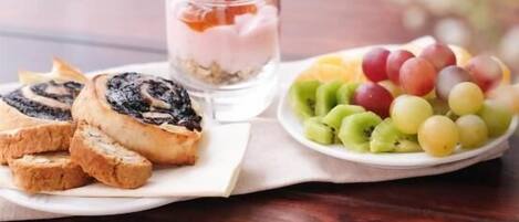 A plate of food including sliced bread, a glass of yogurt with fruit, and a plate of grapes.
