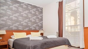 A hotel room with a bed, a nightstand, a window with curtains, and a patterned wall. - König Hotel (Pécs)