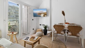 A modern living room with a large TV, wicker chairs, a dining table, and a view of a cityscape through the sliding doors. - Fuengirola Center Rooftop Terrace (Fuengirola)