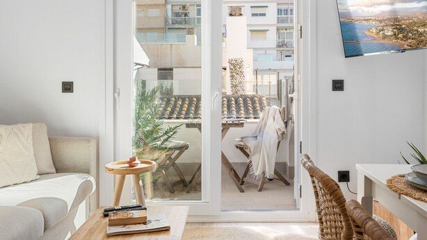 A modern living room with a sliding glass door leading to a balcony, a flat-screen TV mounted on the wall, and a cozy seating area with a sofa and a small round table. - Fuengirola Center Rooftop Terrace (Fuengirola)