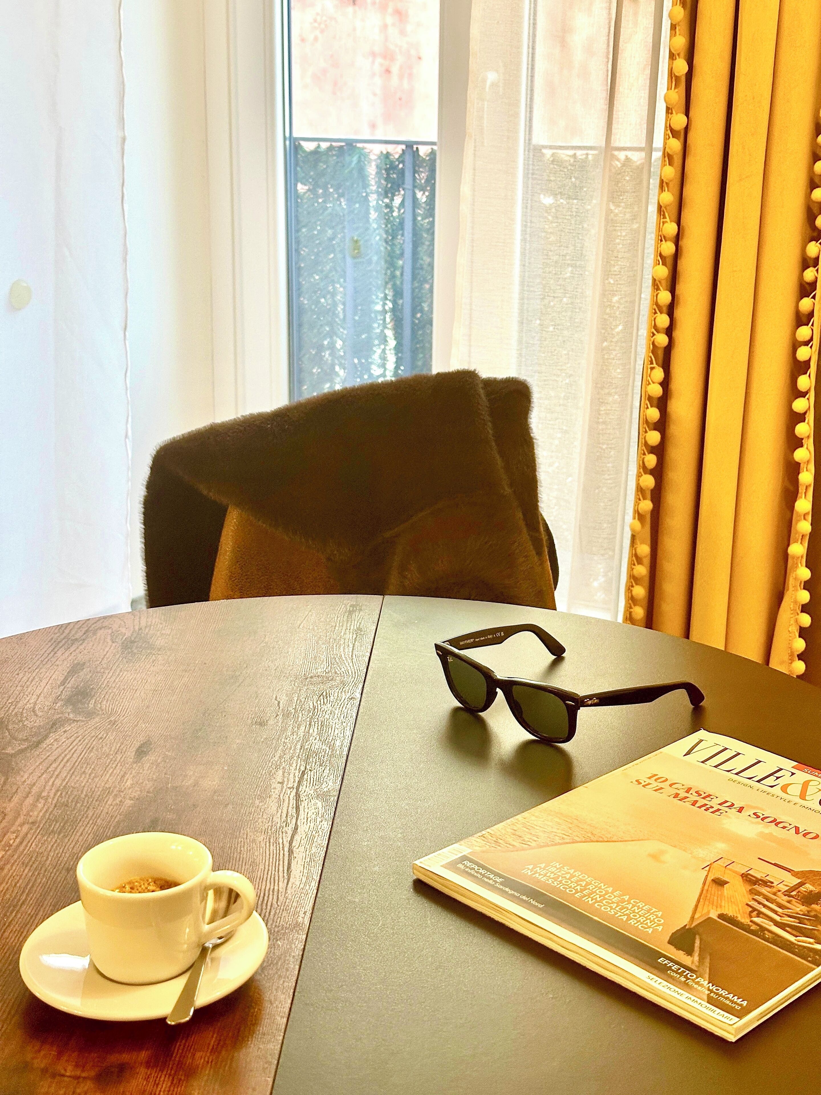 Una mesa con una taza de café, unos lentes de sol y una revista.