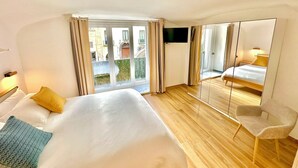 Ein Hotelzimmer mit einem großen Bett, einem Sessel, einem Fernseher und einem Balkon mit Vorhängen.