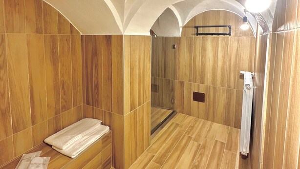 Ein Wellnessraum mit Holzwandverkleidung, einer Glasdusche und einem Handtuch auf dem Boden.