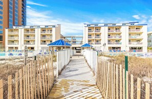 Een pad dat leidt naar een gebouw aan het strand, met meerdere balkons en een zwembad.