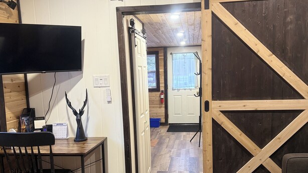 Ein Zimmer mit einem Bett, einem Schreibtisch mit Stuhl, einem Fernseher, einer Holztür und einer Treppe, die in ein weiteres Zimmer führt.