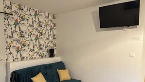 Uma sala de estar com um sofá verde-água, duas almofadas amarelas, um papel de parede estampado, uma televisão na parede e uma pequena mesa de madeira com um controle remoto.