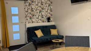 Um quarto com uma mesa redonda, um sofá com almofadas, uma televisão presa à parede e um papel de parede estampado.