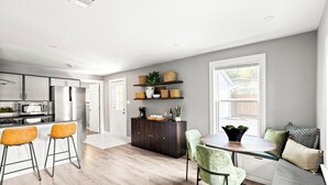 Une cuisine moderne avec un coin repas, dotée d’un plancher en bois, de meubles blancs et d’un four encastré.
