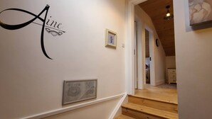 A hallway with a wooden staircase, a framed picture, and a wall-mounted sign that reads "Aline." - Aine Guest House Clonlara (Ruanard)
