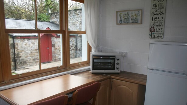 A kitchen with a wooden table, a red chair, a white oven, and a refrigerator. - Aine Guest House Clonlara (Ruanard)